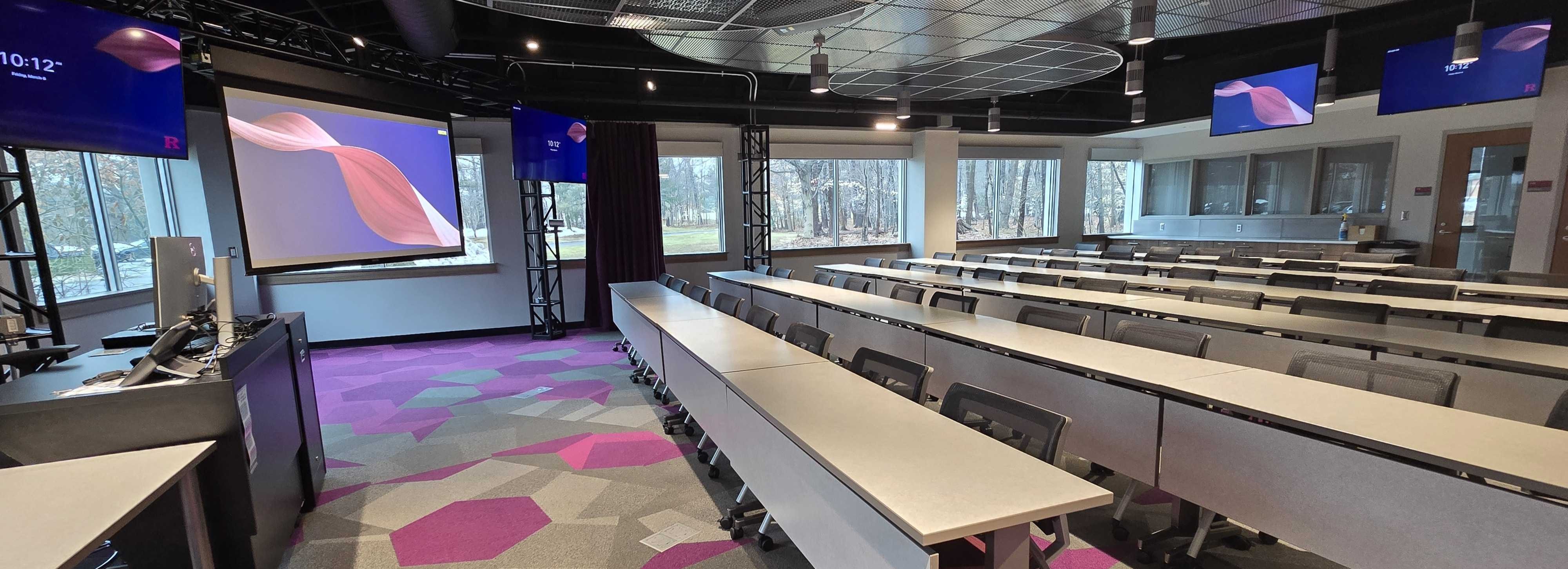 Modern, high technology classroom with a large, lowered front projection screen and monitors around the perimeter of the classroom.s