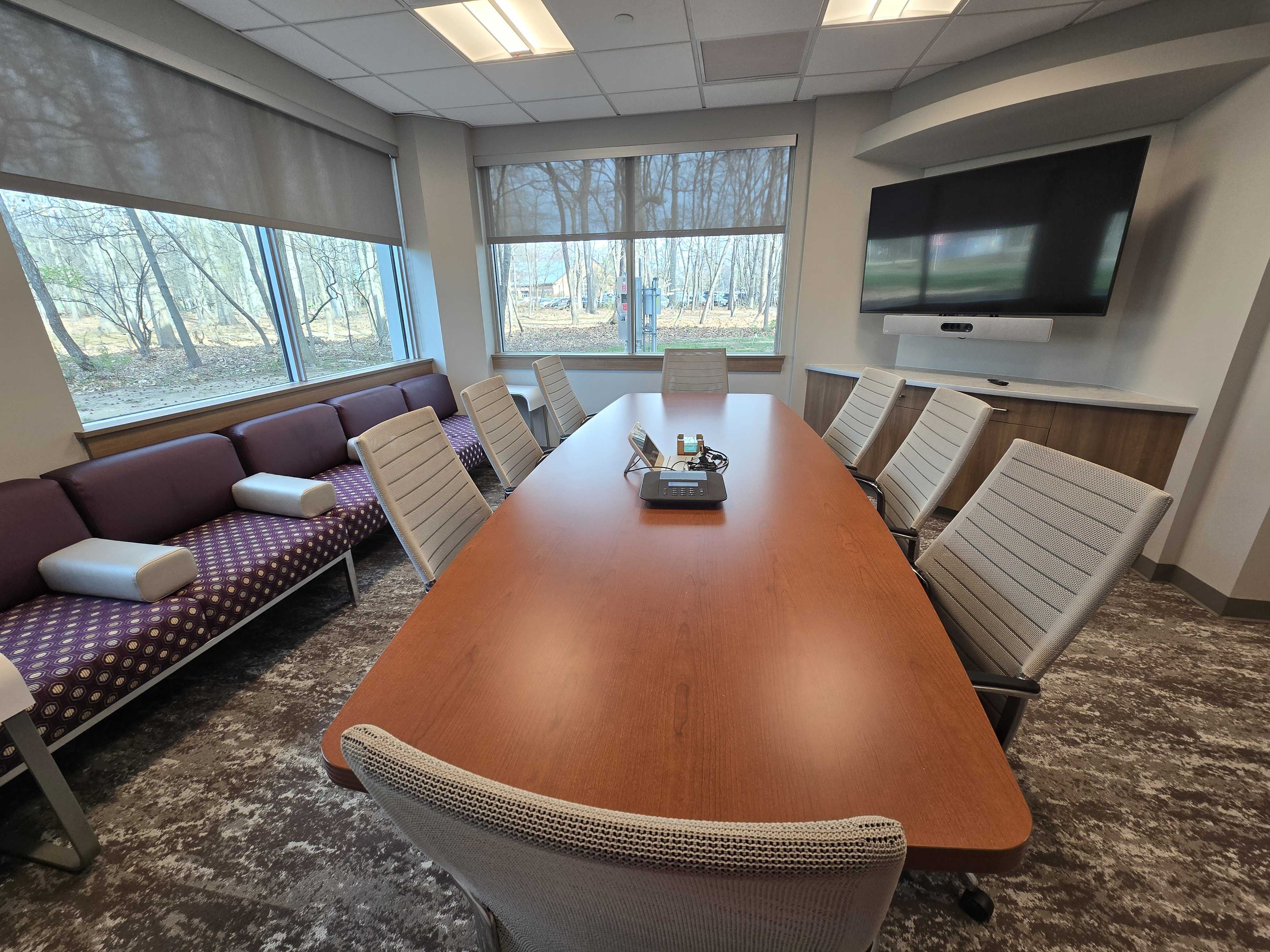 Conference room with a rectangular table in the center with 8 chairs around it and a mounted TV monitor