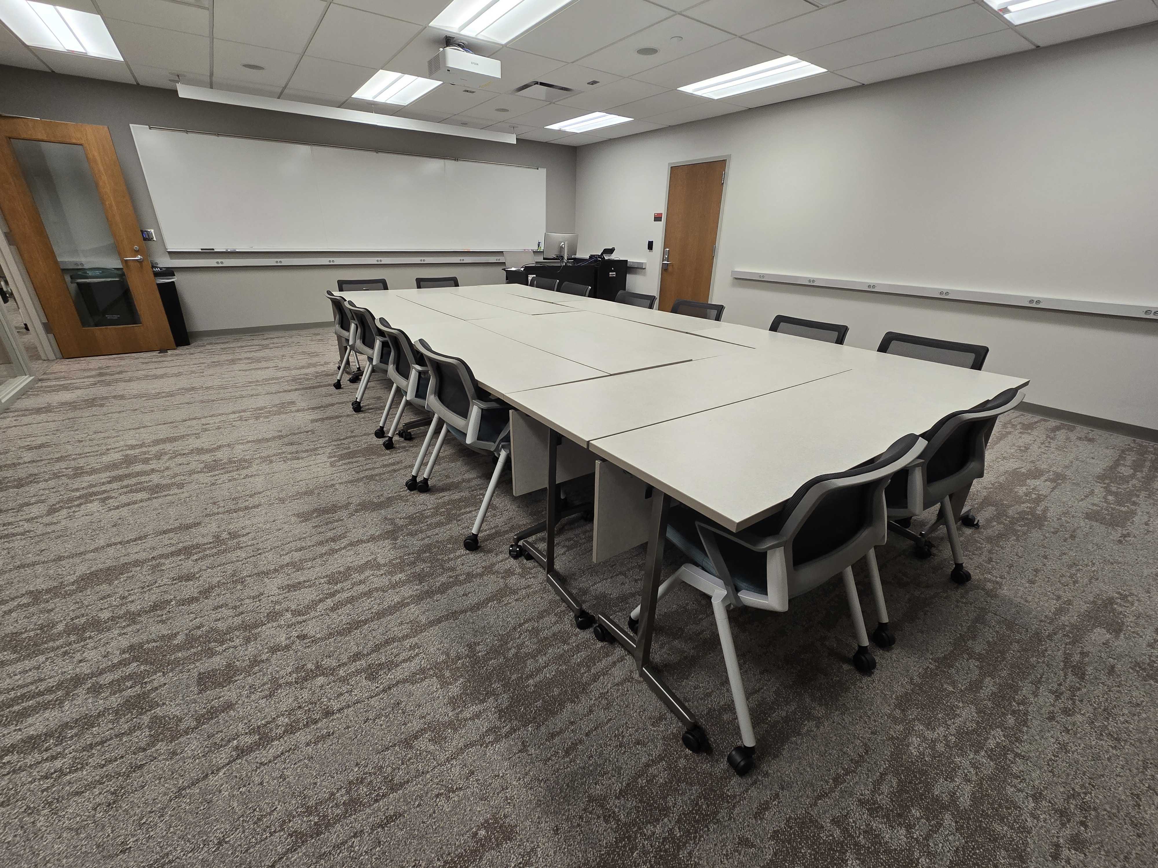 Tables grouped together to form one large rectangular table in the front with chairs around it. 