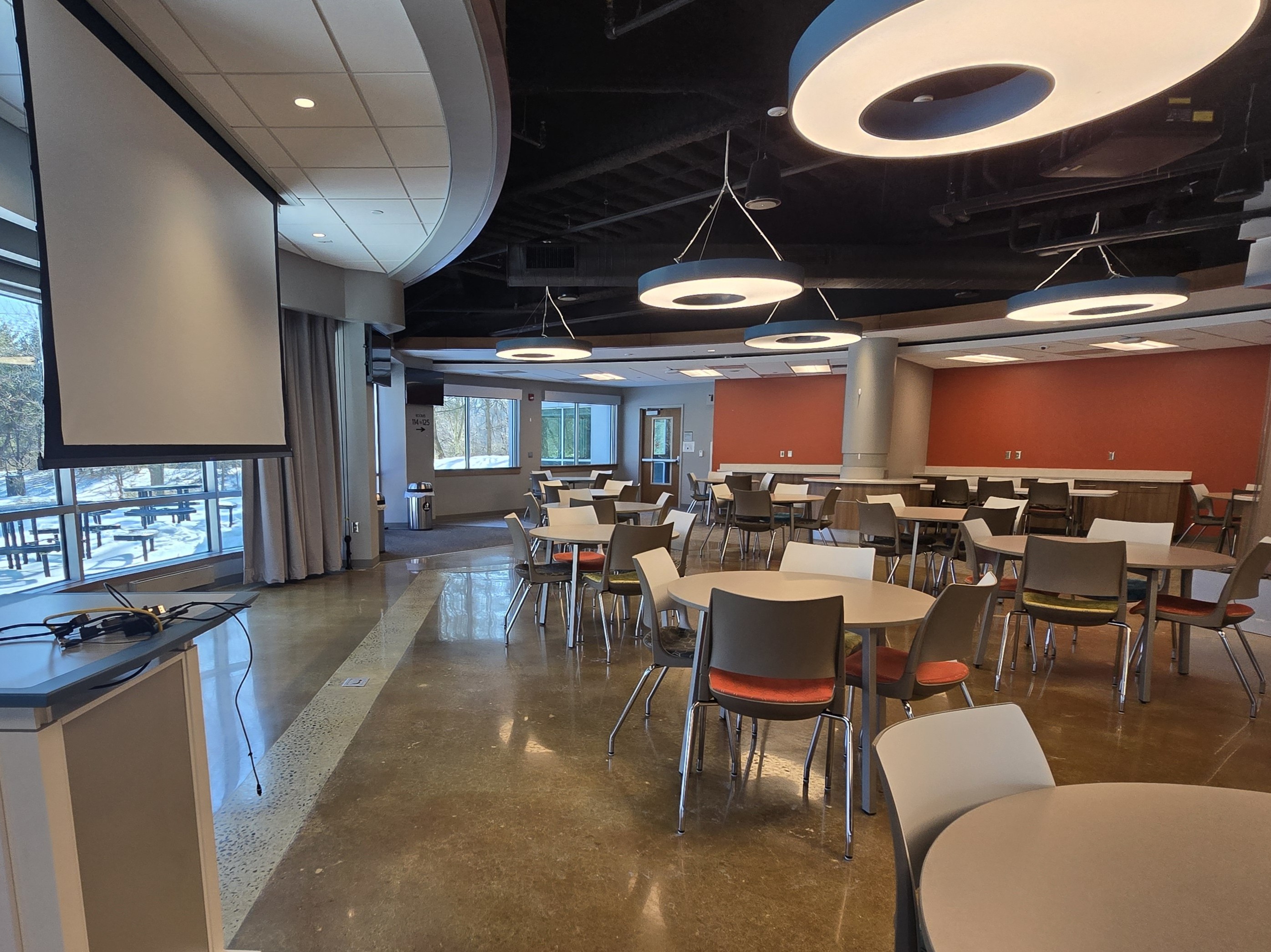 Room with round tables and chairs and a projection screen and podium in the front