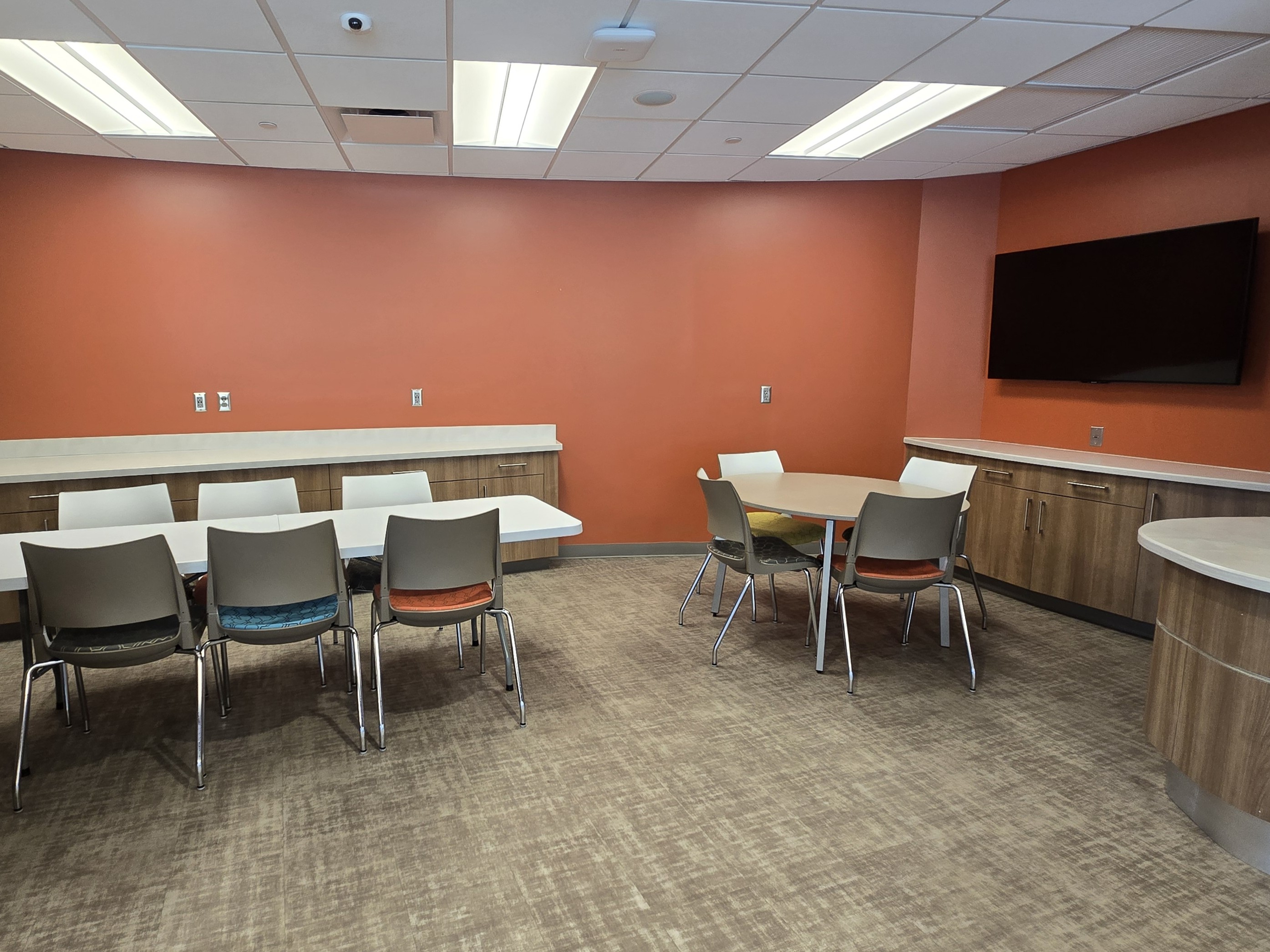 Nook area photo with a rectangular table and round table with chairs and a monitor on the wall.