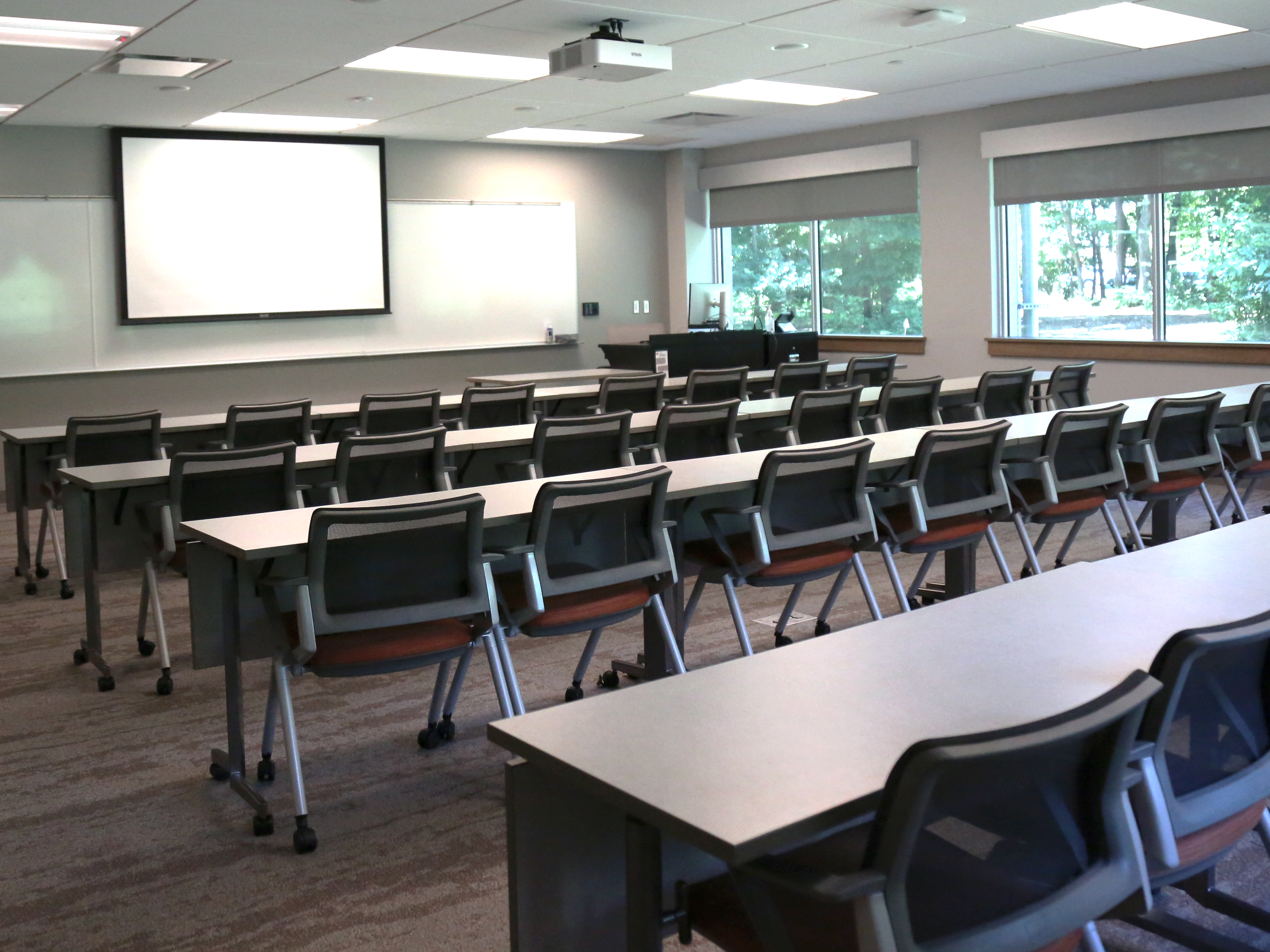 Regular classroom with rows of tables and chairs facing the front whiteboard and projection screen